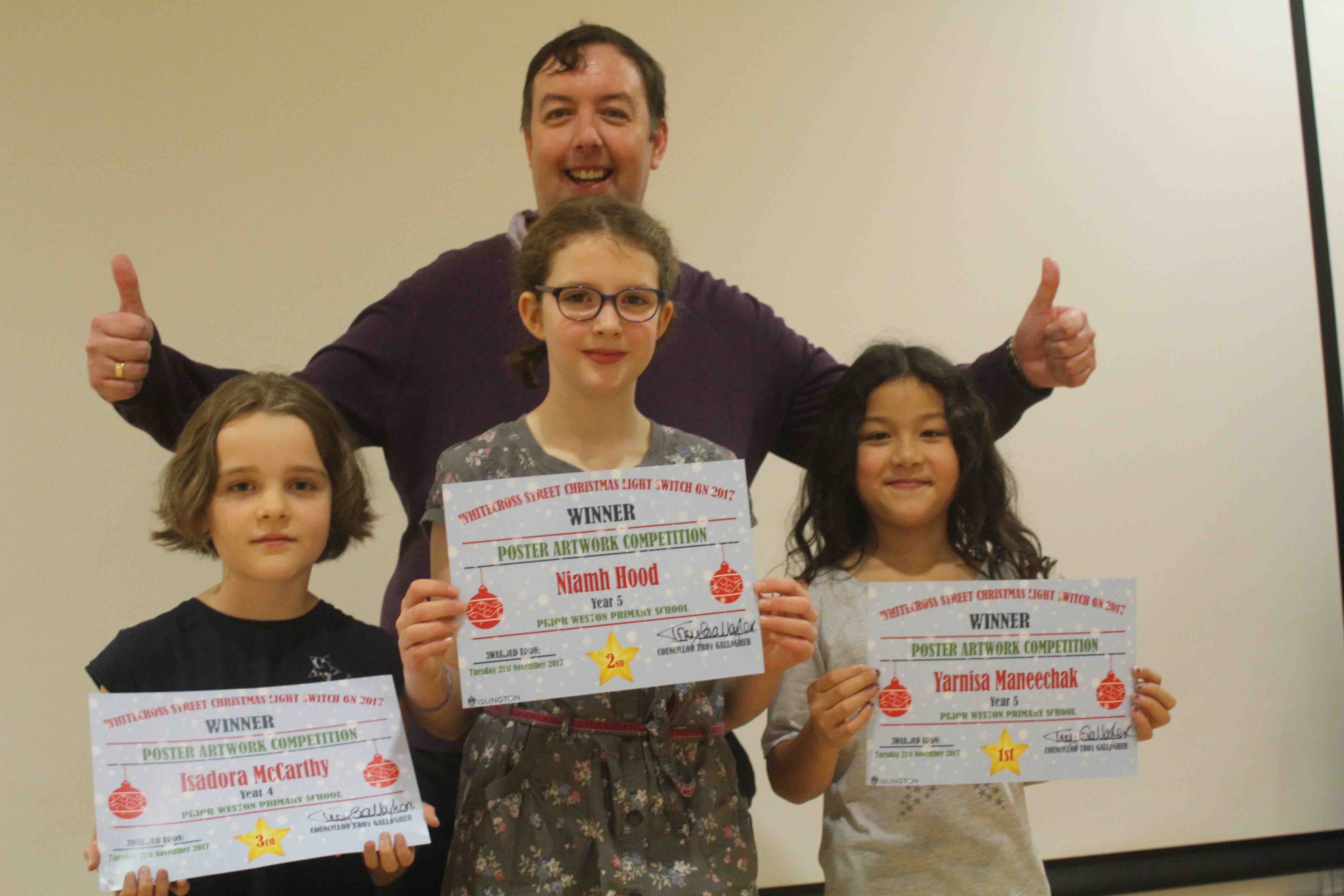 Children design poster for Christmas lights switch-on in Whitecross Street Isadora McCarthy, Niamh Hood and Yarnisa Maneechak with Cllr Troy Gallagher. Left, the winning entry