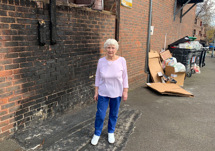 Jean Price in front of damage to her wall shed and fence